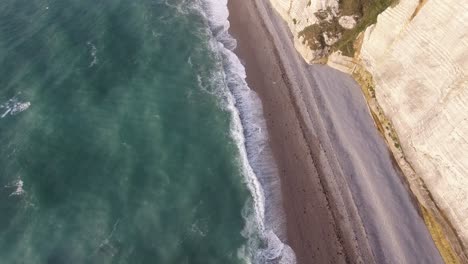 Flying-along-a-beach-with-white-chalk-cliffs-and-arches-at-Etretat-in-Normandy.