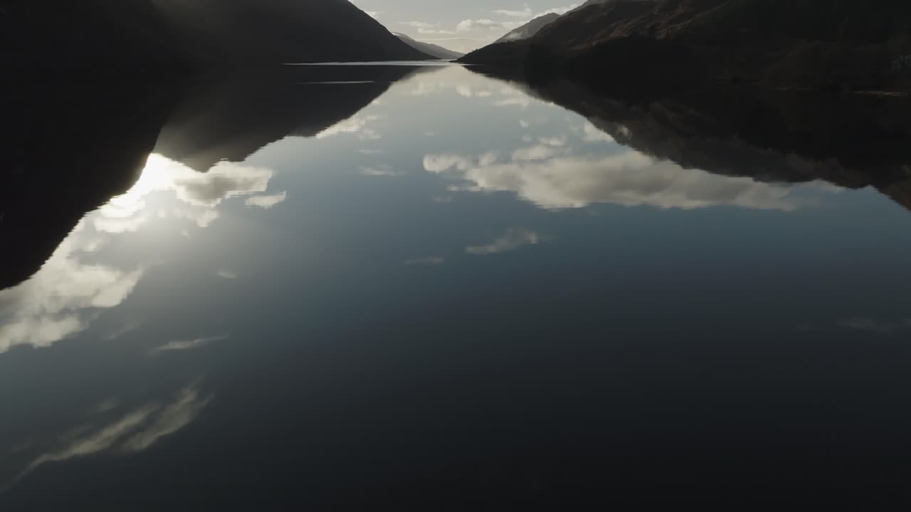 Tilt shot of Isle of Skye mountains mirrored in water beneath a dramatic, cloud-filled sky