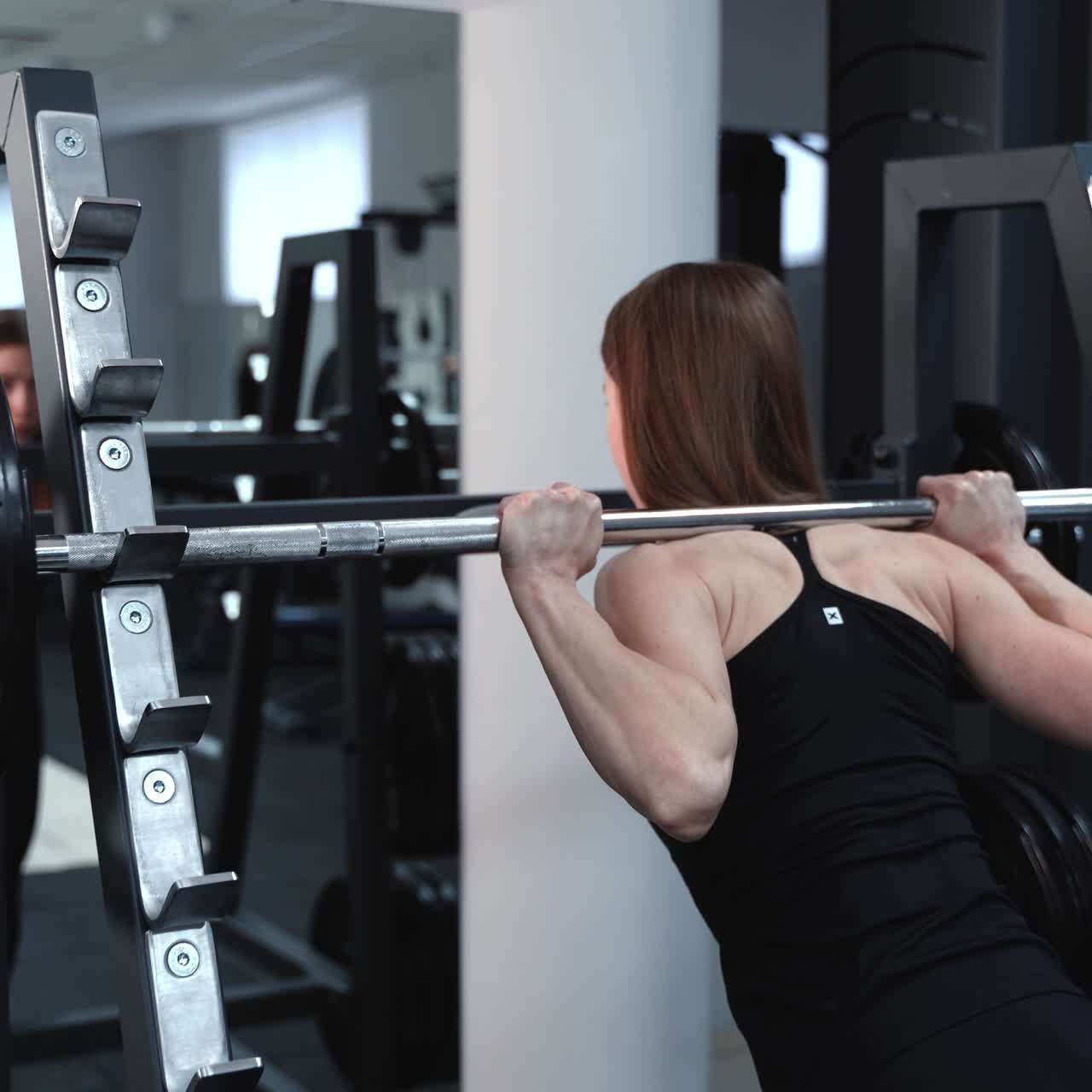 Athletic young woman walks up to the weight bar and lifts her in the fitness club opposite the mirror. Endurance exercise