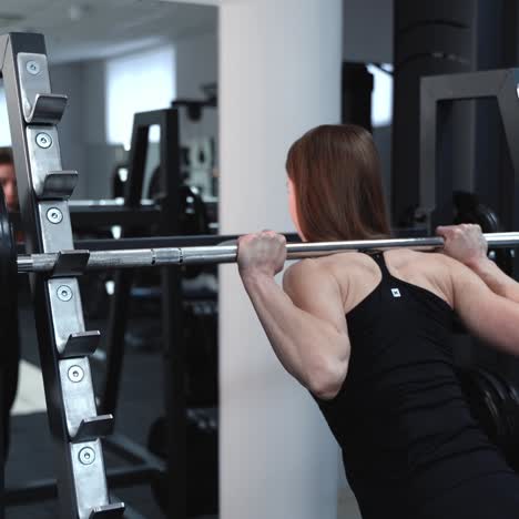 athletic young woman walks up to the weight bar and lifts her in the fitness club opposite the mirror. endurance exercise