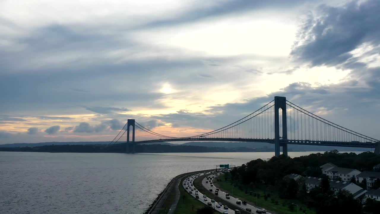 An aerial view over the Belt Parkway in Brooklyn, NY. The drone camera starts low and raises altitude during a sunset creating a time lapse with the Verrazzano Bridge in the background