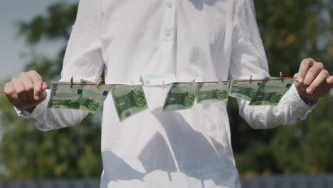 A-man-holds-a-clothesline-in-his-hands,-on-which-banknotes-hang.-Money-laundering-concept.-Low-angle-shot