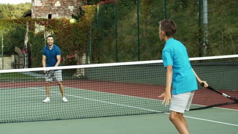 rear view of a teen boy playing tennis with his dad and losing the match