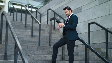 Businessman-laughing-with-phone-in-hand-at-street.-Man-using-smartphone-outdoor