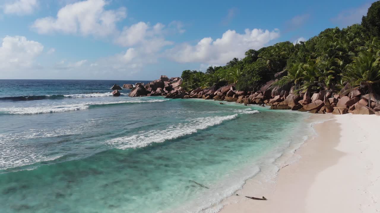 vista aérea siguiendo las olas rodando hacia las playas blancas y despobladas de anse coco, petit anse y grand anse en la digue, una isla de las seychelles