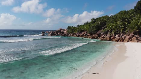 aerial view following the waves rolling towards the unpeopled, white beaches at anse coco, petit anse and grand anse on la digue, an island of the seychelles