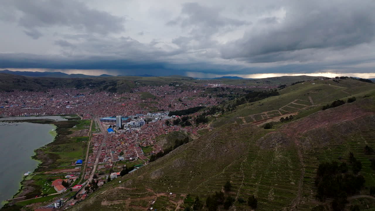 Vista aérea cinematográfica de drone da cidade de Puno, nas margens do Lago Titicaca. A extensa paisagem urbana tem como pano de fundo a Cordilheira dos Andes sob um céu nublado e dramático, Peru