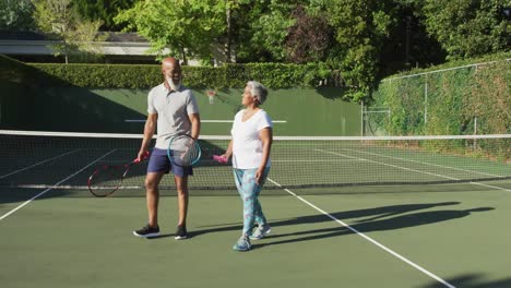 Pareja-De-Ancianos-Afroamericanos-Sosteniendo-Raquetas-Hablando-Entre-Sí-En-La-Cancha-De-Tenis