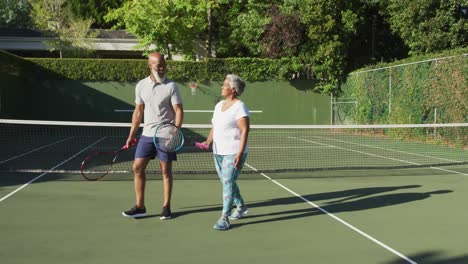 african american senior couple holding rackets talking to each other on the tennis court