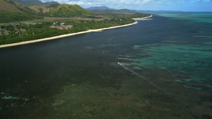 Kiteboarding in shallow waters of Poe's Beach near Domaine de Deva, New Caledonia - aerial