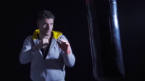 boxer young man punching punching bag in dark gym.