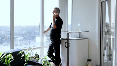 hombre tomando el teléfono móvil mientras está de pie cerca de la ventana 4k