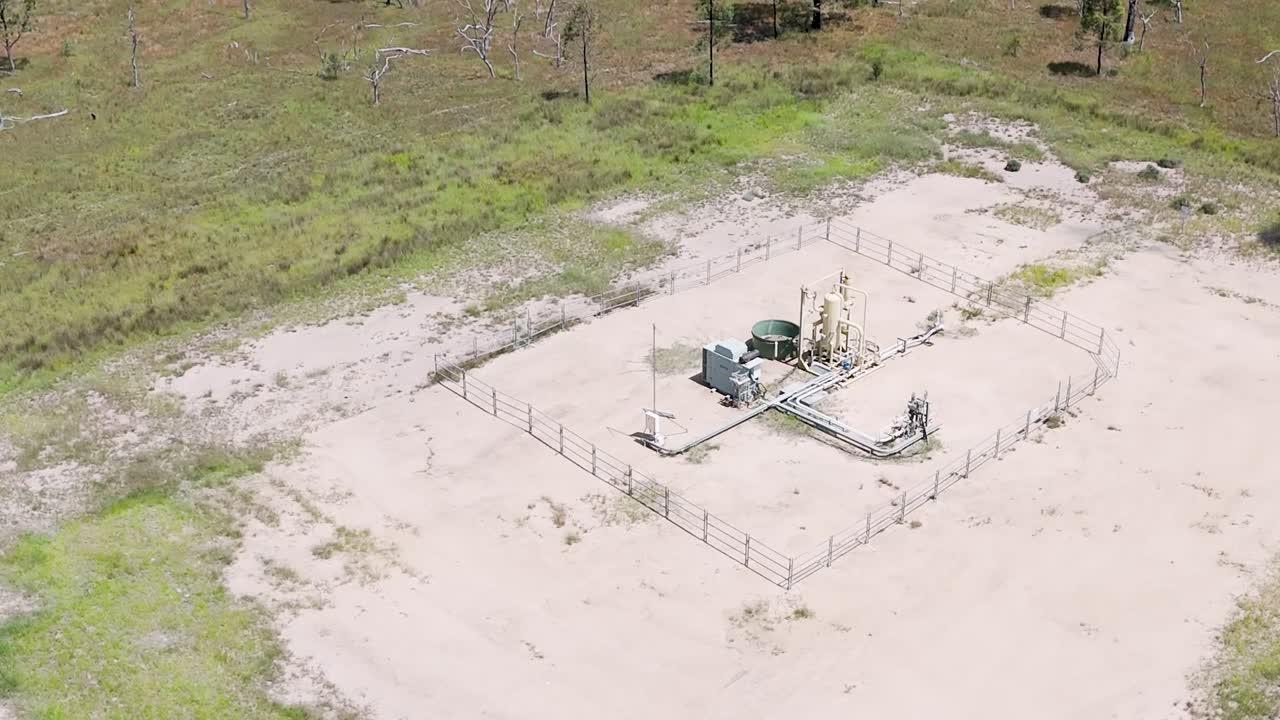 Aerial view of a small, fenced gas extraction site surrounded by open land and sparse vegetation.