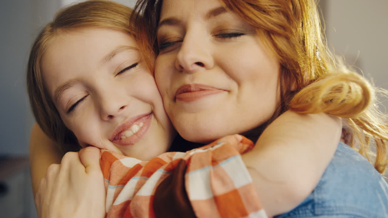 Close up of the cute happy girl with her mother hugging and telling each other how much they love each other. Portrait shot. Indoor