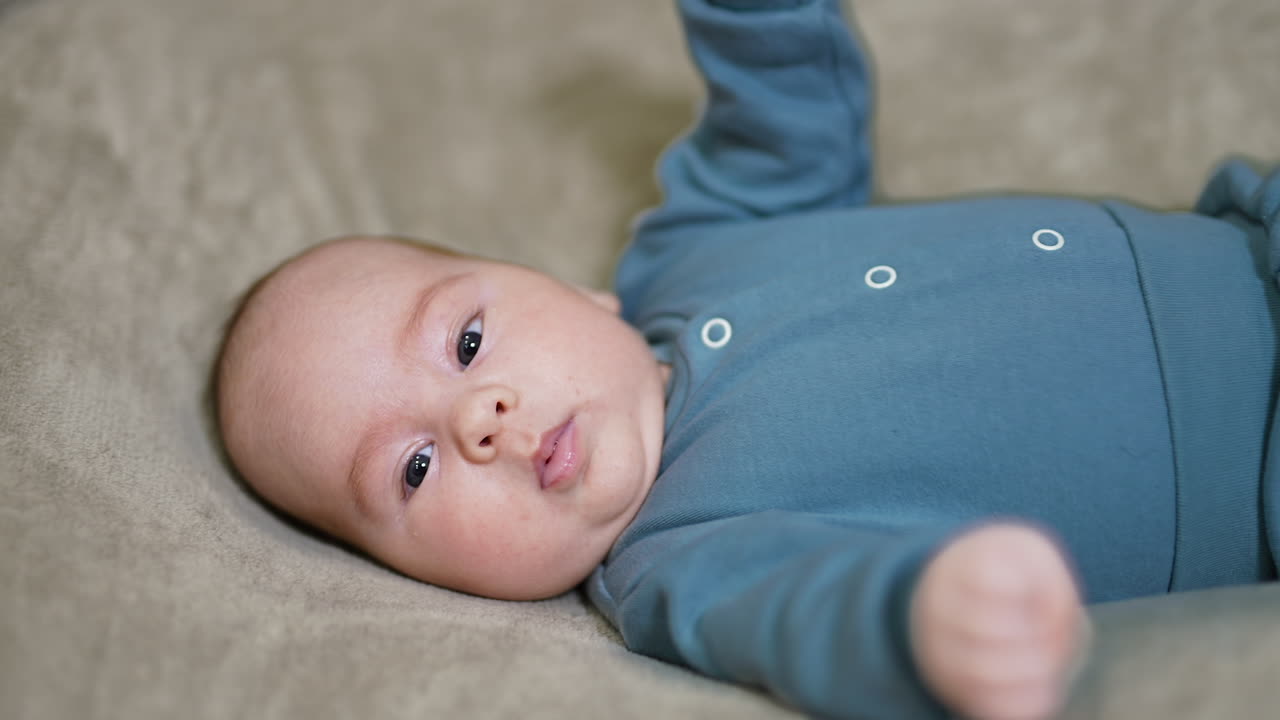 Lovely baby boy with cute plump cheeks lies on his back with his head to a camera. Grey blanket backdrop.