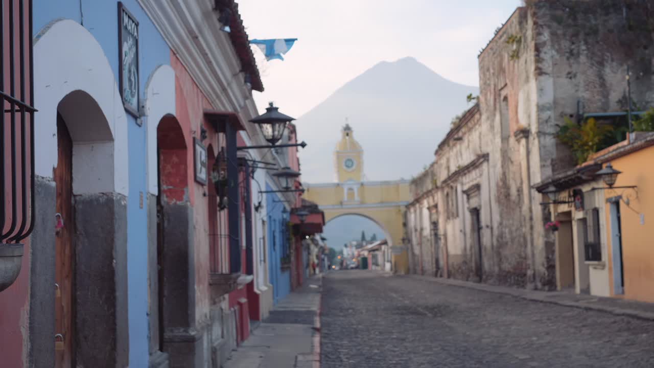 Ung, smuk, blond rejsende pige med blå øjne udforsker den gamle koloniby Antigua, Guatemala, med Santa Catalinas klokketårn synligt.