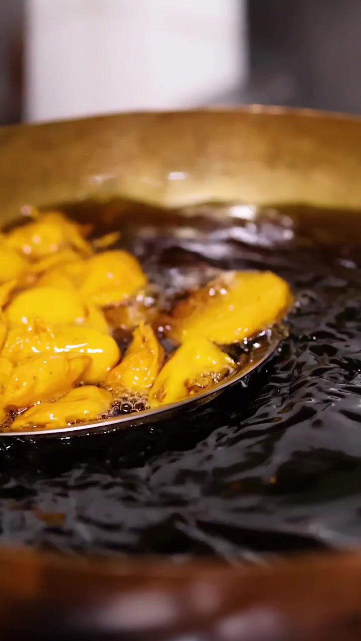 Close-up of golden fritters frying in bubbling oil within a traditional brass wok.