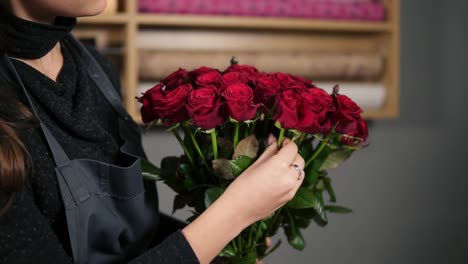 Focus-on-the-bunch-of-red-roses:-young-attractive-female-florist-arranging-bouquet-of-beautiful-red-roses-at-flower-shot