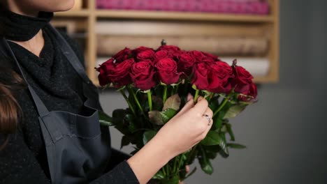 focus on the bunch of red roses: young attractive female florist arranging bouquet of beautiful red roses at flower shot