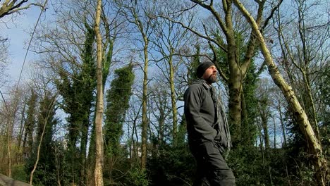 low angle follow shot of male in hat - scarf walking through sunny cold woodland trees