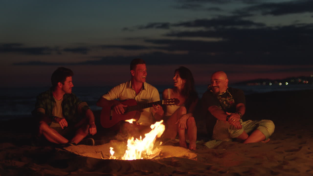 amigos disfrutando de música y fogata en la playa por la noche