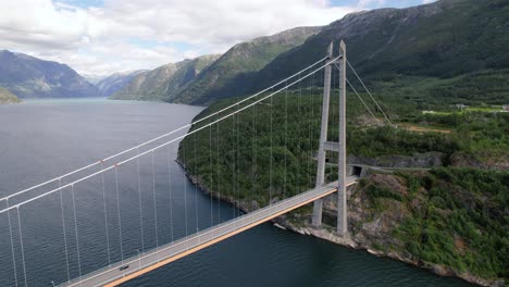 aerial view of a car passing through hardangerbrua suspension bridge above calm fjord seawater on a cloudy day