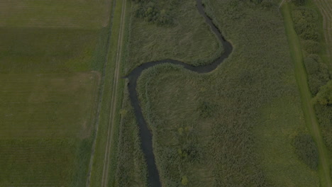 vuelo aéreo sobre un río sinuoso a través de tierras de cultivo cubiertas de hierba en debki, polonia