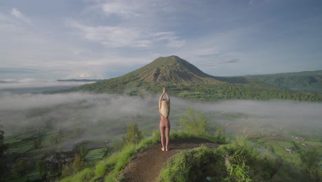 在batur山的kayupadi觀點上,一個瑜伽女士練習向上致敬,舉起雙手姿勢