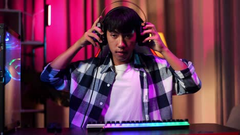 front view of asian teen boy gamer wearing head phones and start play video game on computer