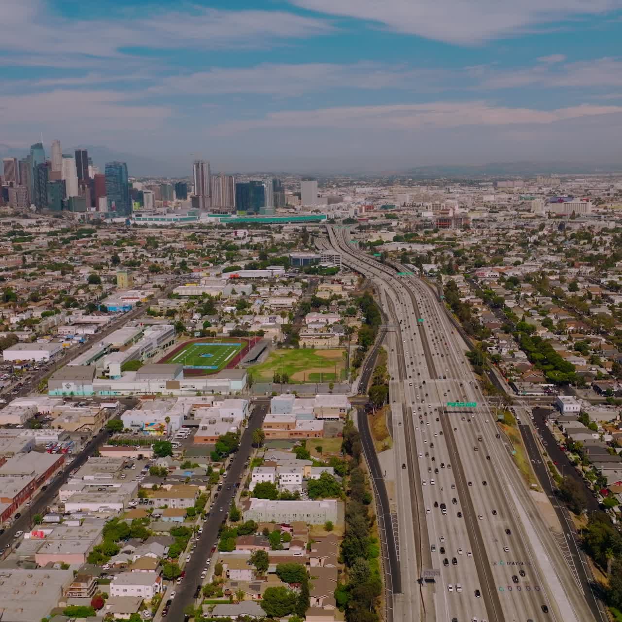 Wide busy road with numerous cars moving to and from financial downtown. Beautiful skyscrapers standing out at backdrop of blue cloudy sky