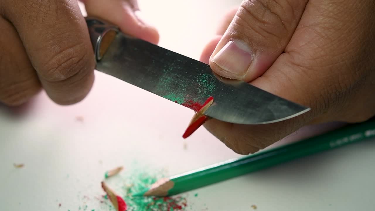 Opptak av hender som sakte spisser en blyant og noen fargeblyanter med en skarp kniv