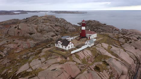 Wunderschöne-Insel-Ryvingen-Mit-Aktivem-Leuchtturm-Und-Leuchtturmwärterhaus-Außerhalb-Von-Mandal,-Norwegen-–-Luftaufnahme,-Die-Sich-Langsam-Dreht-Und-Von-Der-Nähe-Zum-Überblick-über-Den-Standort-Bewegt