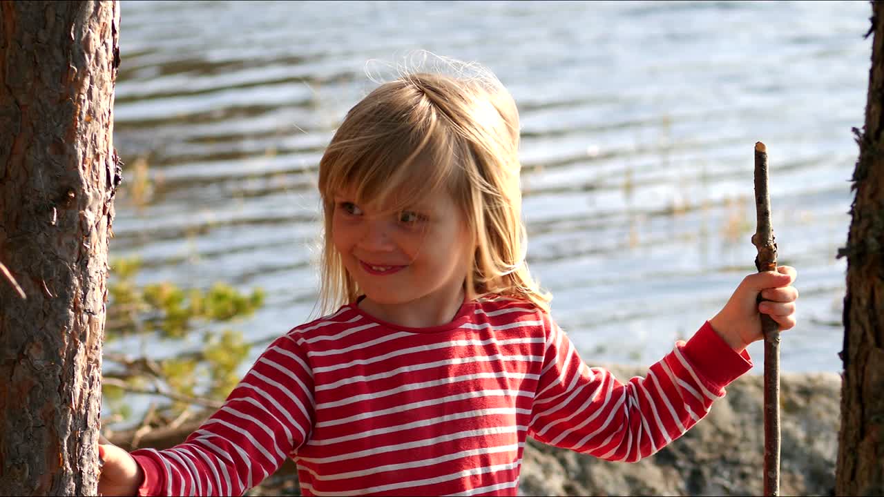 Portret szczęśliwej, uroczej dziewczynki trzymającej patyk nad wodą, w zwolnionym tempie.