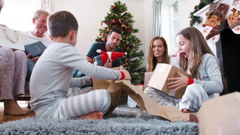 three generation family wearing pajamas in lounge at home opening gifts on christmas day