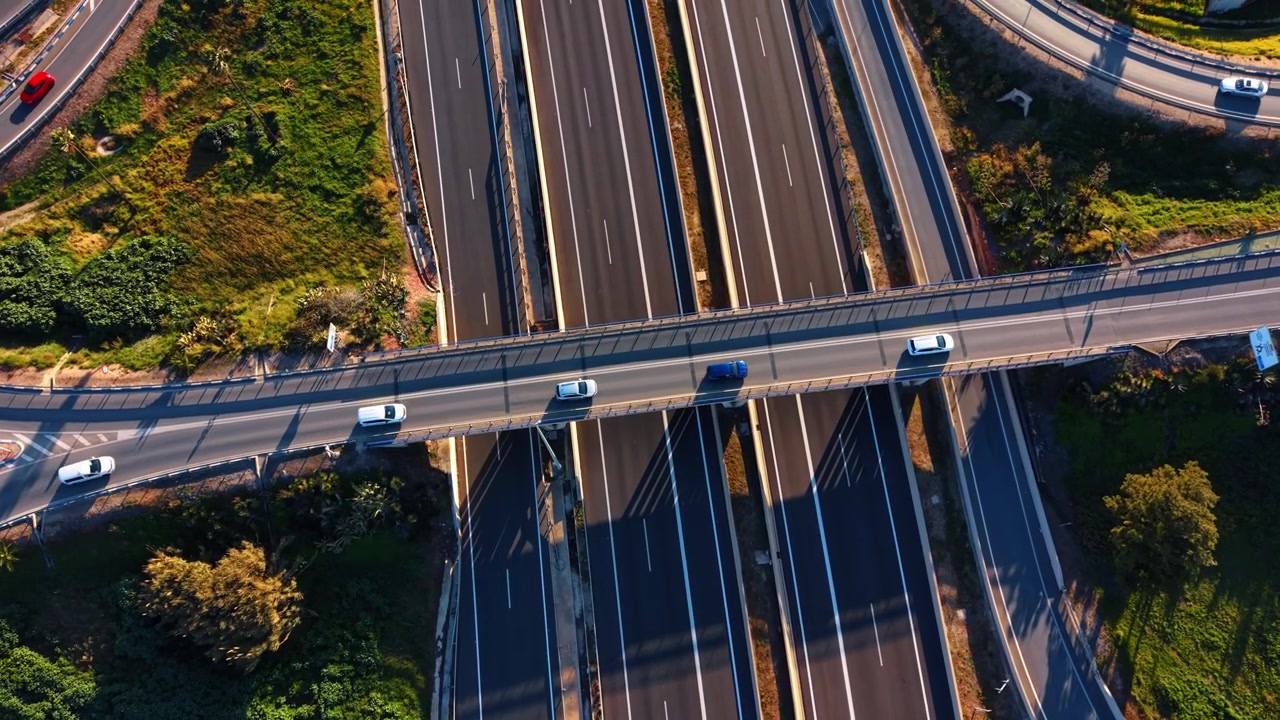 Luftaufnahme einer Brücke, die eine mehrspurige Autobahn überquert, Spanien. Drohnenaufnahme von oben mit Fahrzeugen, die lange Schatten auf dunklen Asphalt werfen.