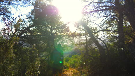 Man-walking-through-the-mountains-with-trees-and-sunset-in-the-background-in-the-early-morning