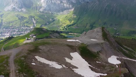 Toma-De-Drones-De-Una-Estación-De-Esquí-En-Verano-Con-Montañas-En-El-Fondo-Y-Parches-De-Nieve