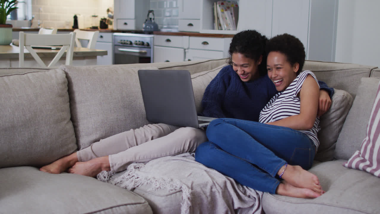 Mixed race lesbian couple sitting on couch embracing and using laptop