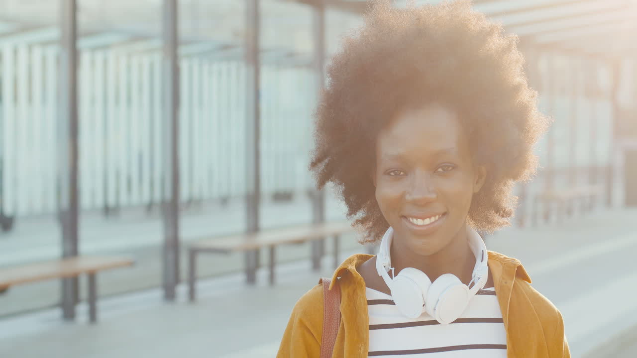 Close-up view of african american woman traveller in headphones smiling and looking at camera at bus station