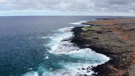 drone view of rugged volcanic coastline blending into turquoise ocean waves along mahana beach, hawaii. striking contrast of lava rock, surf, and overcast sky.