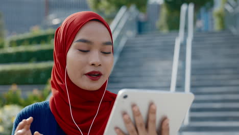young muslim woman in hijab using a tablet and earphones outdoors
