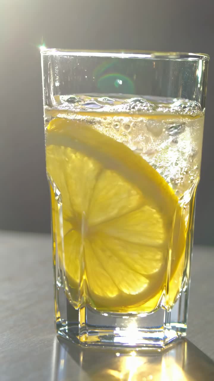 Primo piano di una fetta di limone rinfrescante in un bicchiere d'acqua, retroilluminata dalla luce del sole