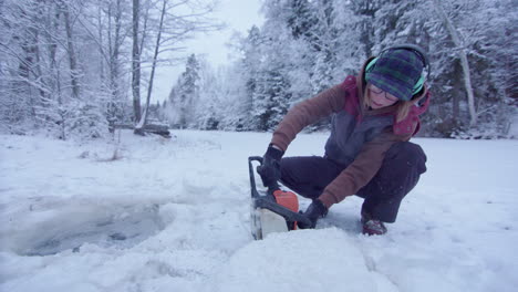 portátil: una mujer que usa una motosierra corta dramáticamente un agujero en el hielo