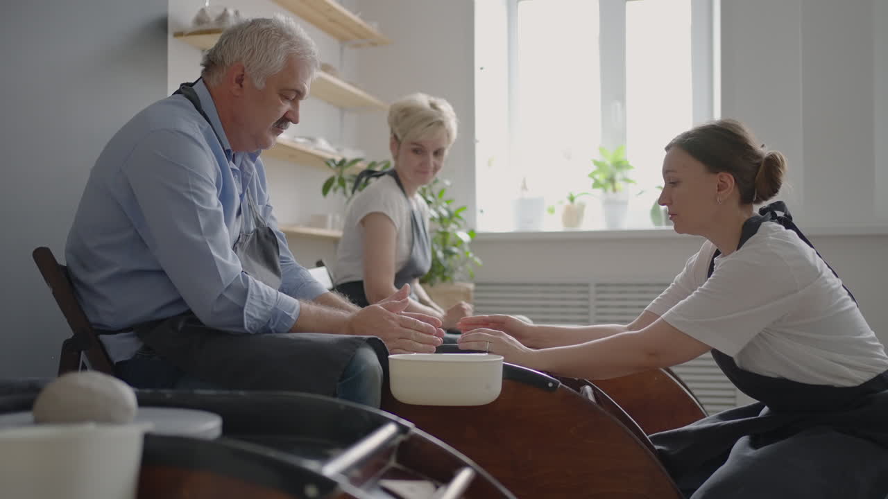 A group of senior women and a man together learn to make pottery on a potter's wheel. Making utensils on a retired potter's wheel