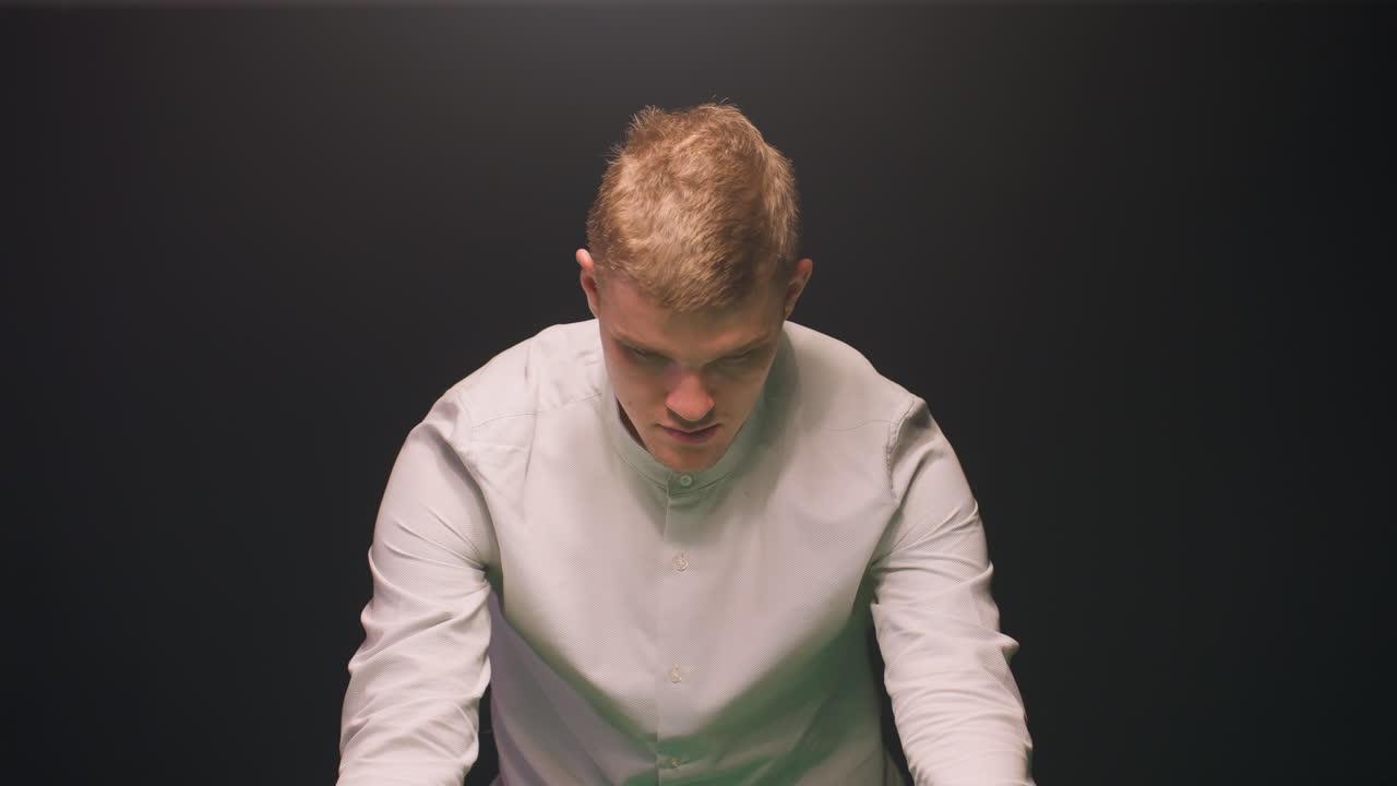 primer plano de un joven con una camisa blanca, profundamente enfocado con una concentración tranquila contra un fondo oscuro. la luz aérea arroja un brillo suave, enfatizando su expresión compuesta