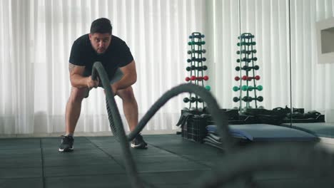 Hombre-Usando-Cuerdas-De-Batalla-Para-Azotar-Ejercicio-En-Un-Gimnasio-En-Cámara-Lenta