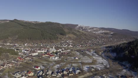 Drone-view-of-Padure---community-in-valley-below-mountains-lined-with-pine-trees