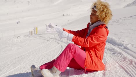 Frau-Im-Orangefarbenen-Schneeanzug-Sitzt-Auf-Der-Skipiste