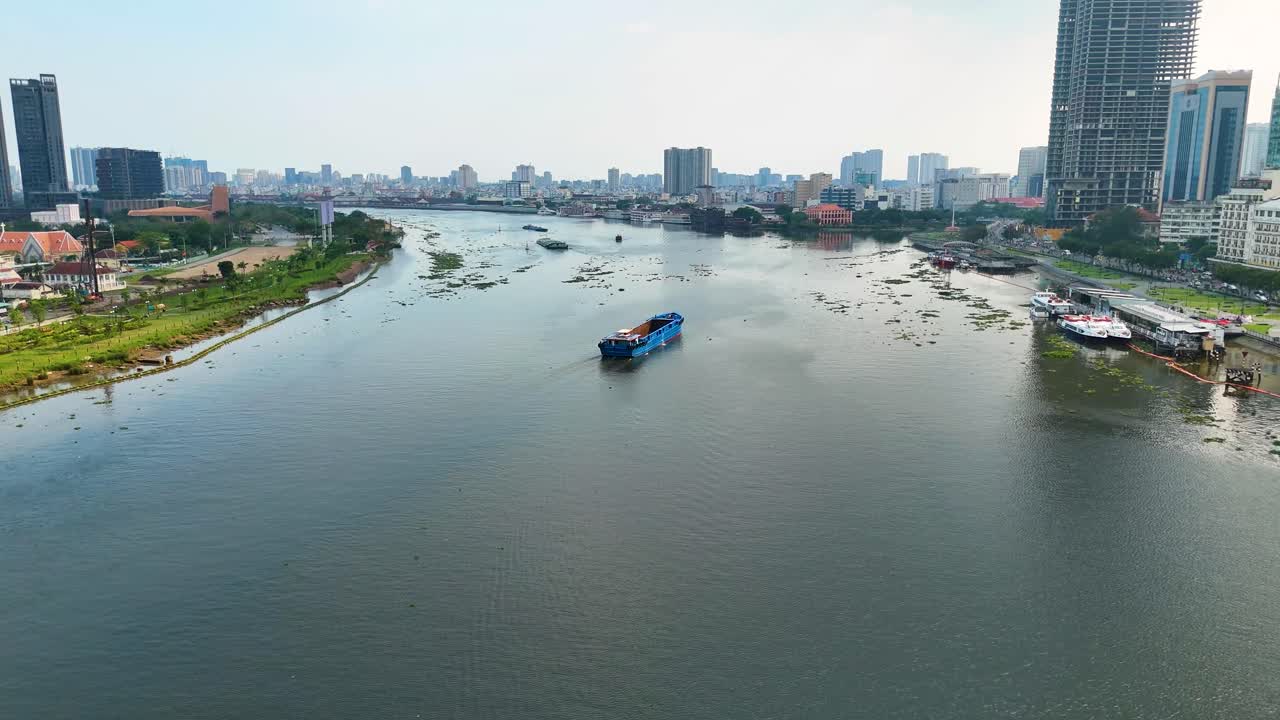 An empty freighter barge on the Saigon River in Ho Chi Minh City, cruising past skyscrapers, Vietnam