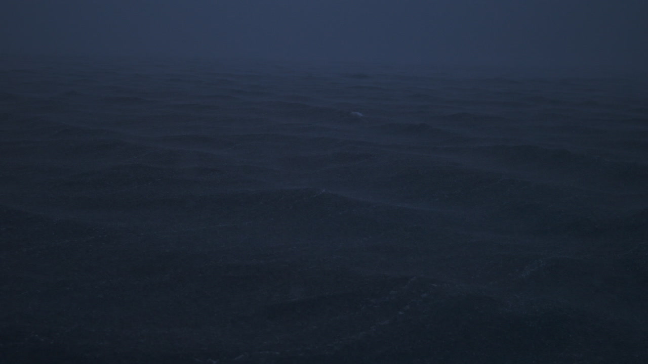 Slow-motion of rain hitting deep gray waves under thick storm clouds